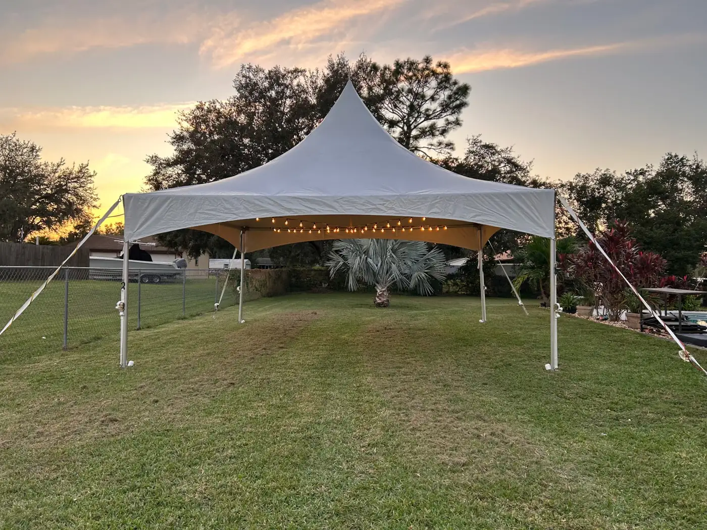 White high-peak tent with string lights on a lawn at sunset