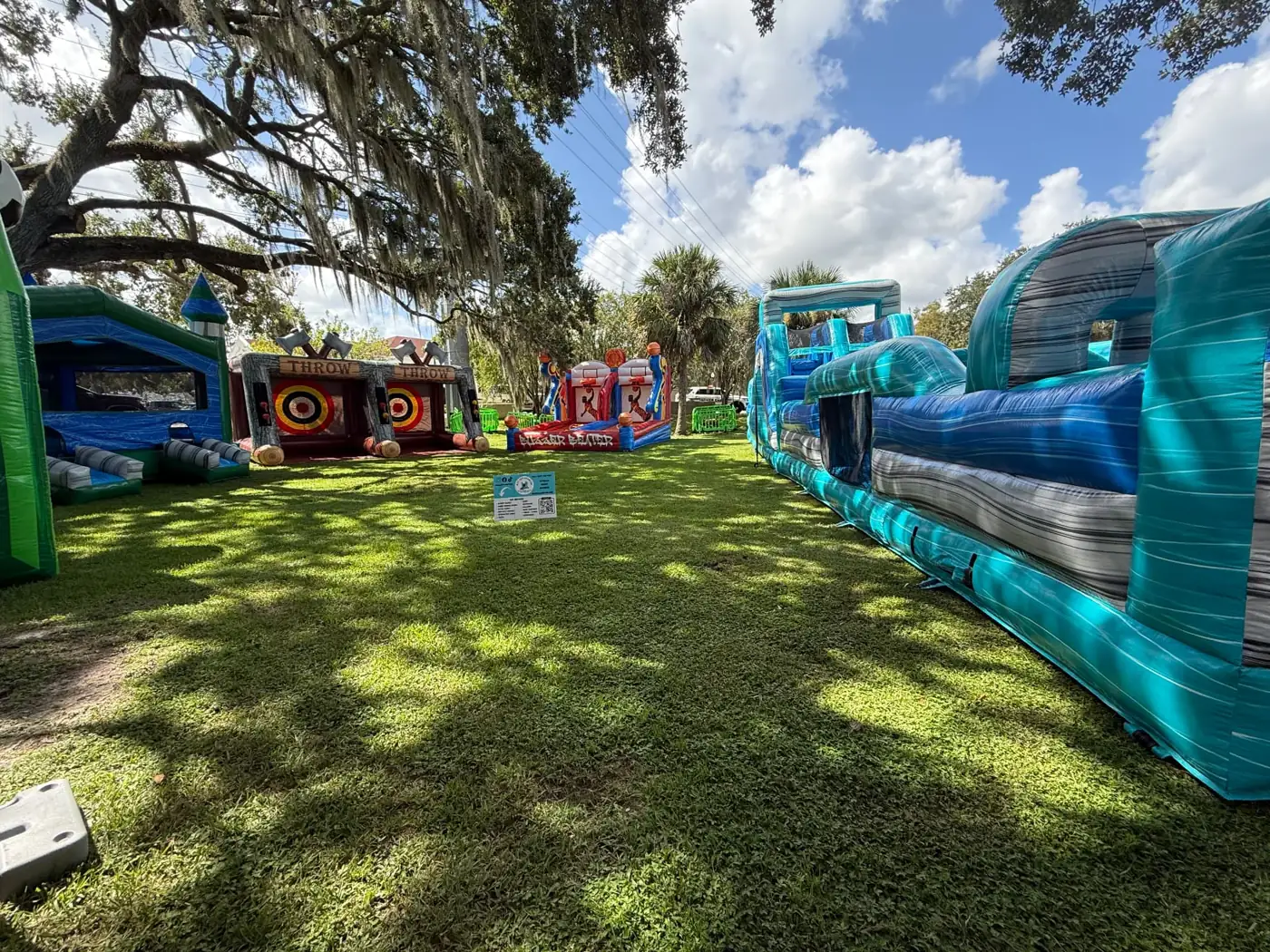 Blue inflatable obstacle course and sports games arranged beneath trees