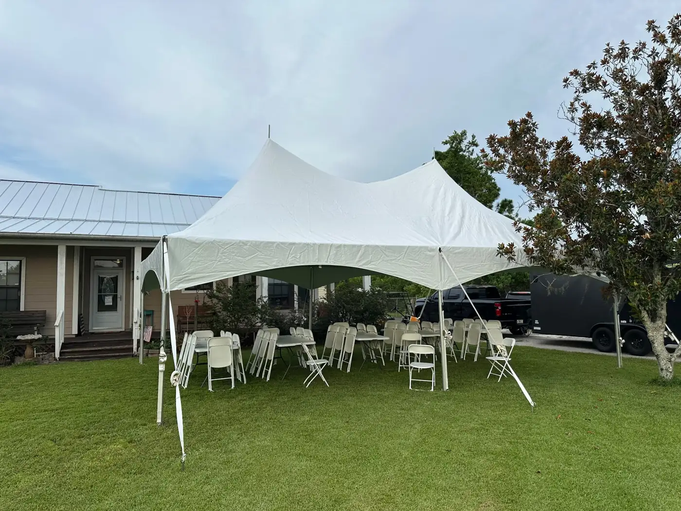 White peaked tent sheltering tables and chairs beside a home