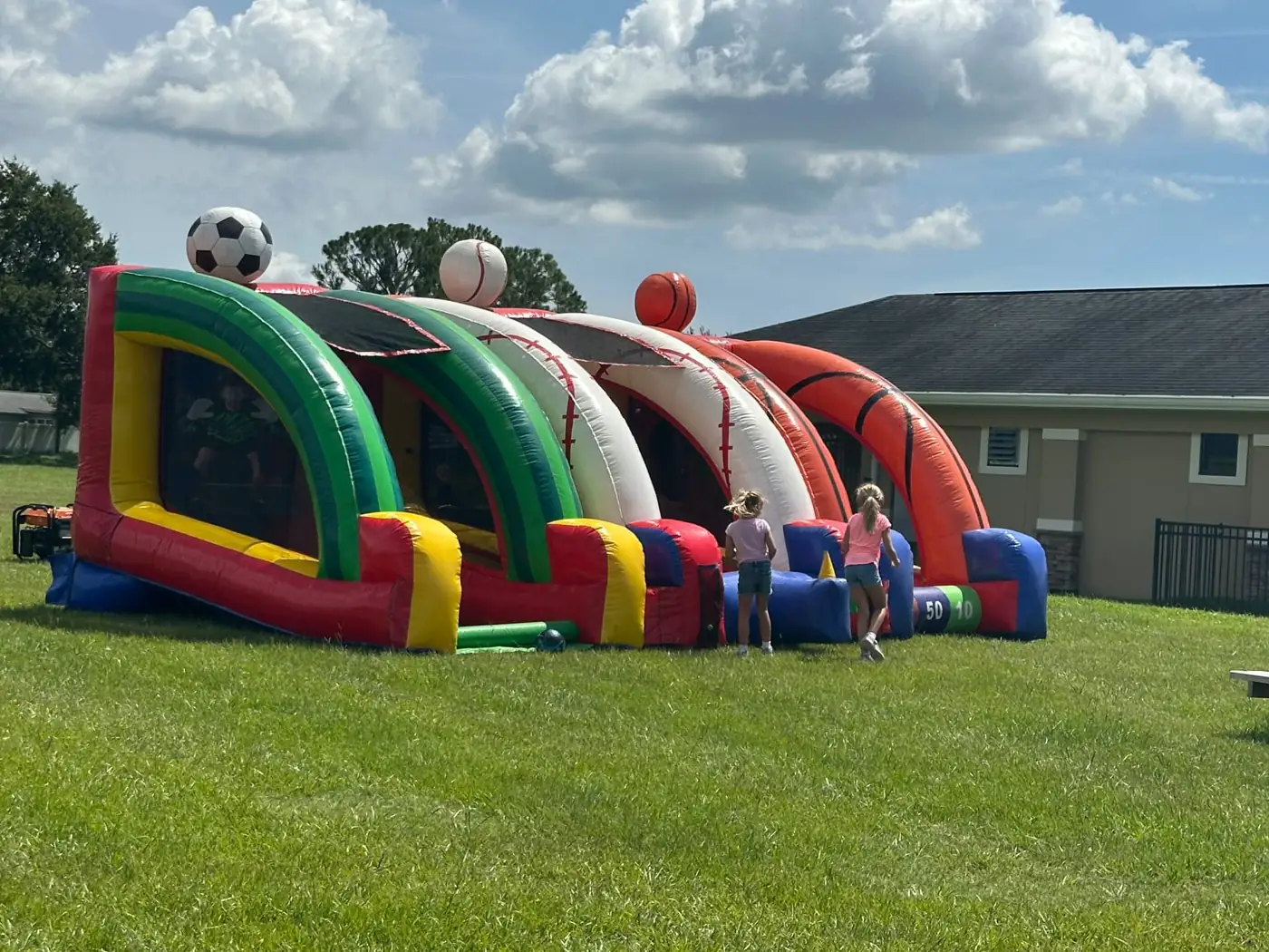 Colorful sports-themed bounce house with slide on a lawn
