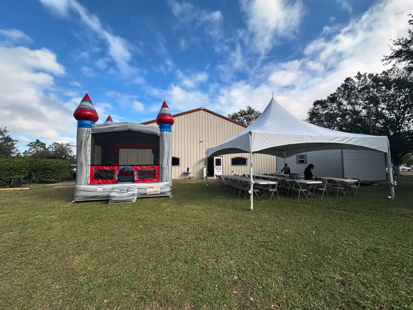 White event tent with tables and chairs beside a castle bounce house