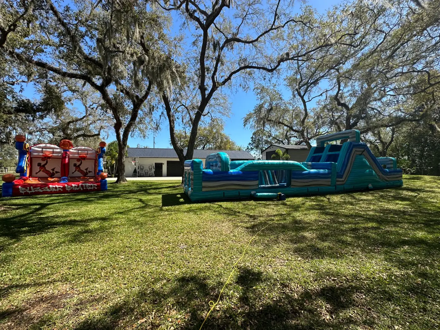 MJT inflatable obstacle course and games set up on grass beneath trees