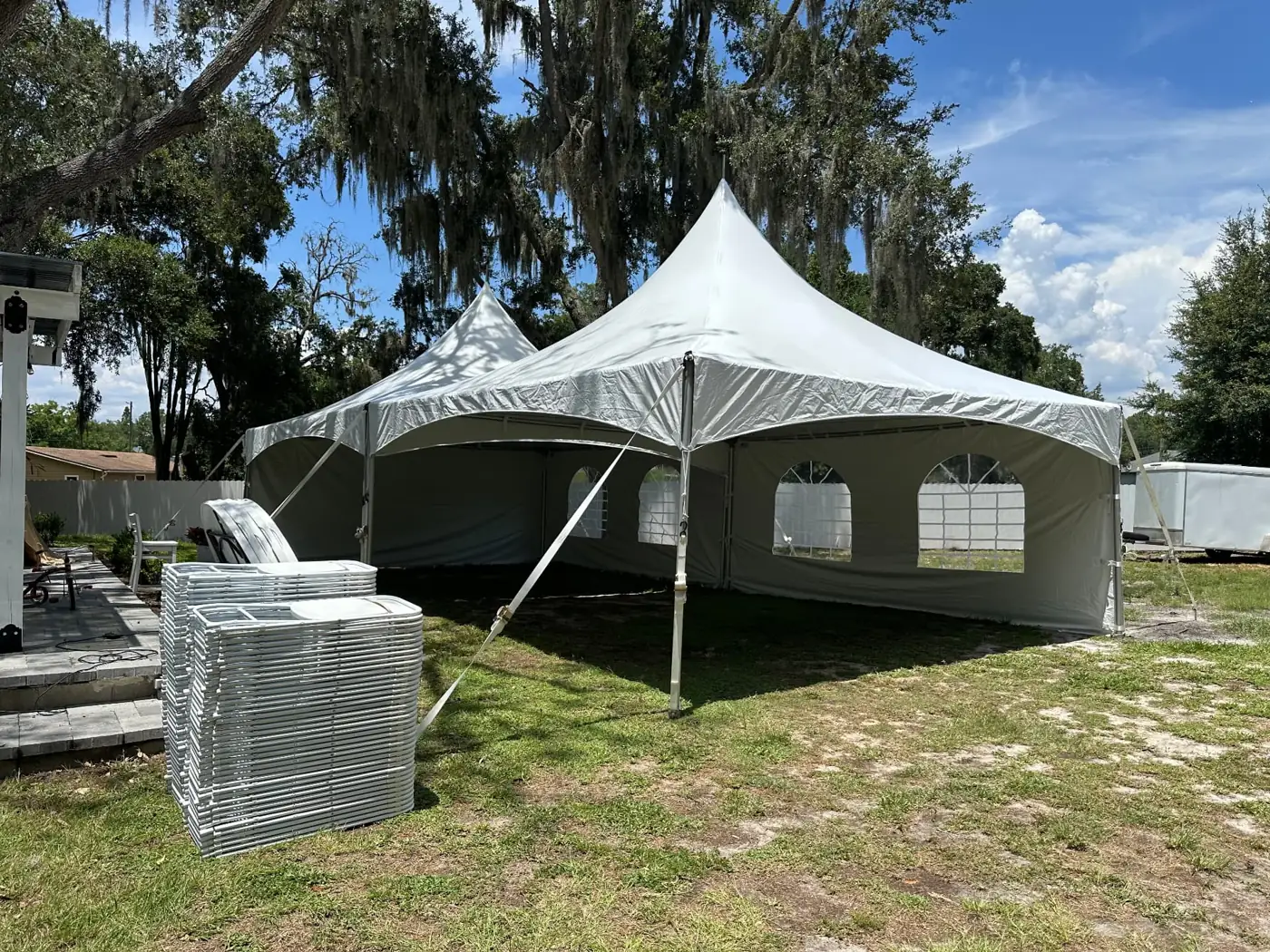 White peaked tent with windowed sidewalls beside a tree