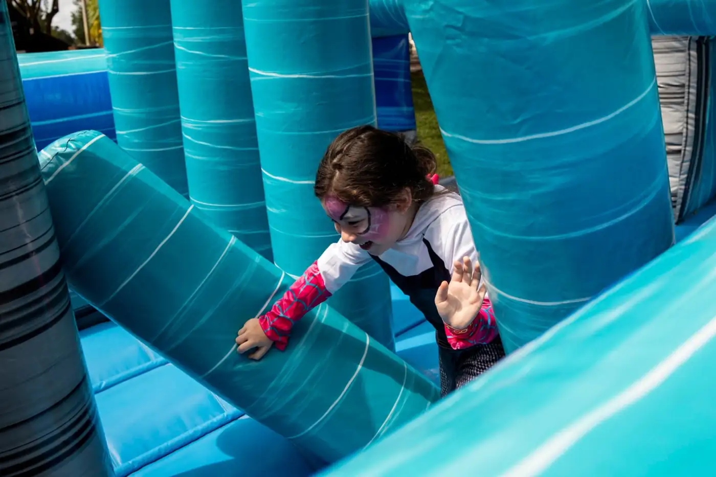 Child moving between blue inflatable obstacle-course pillars